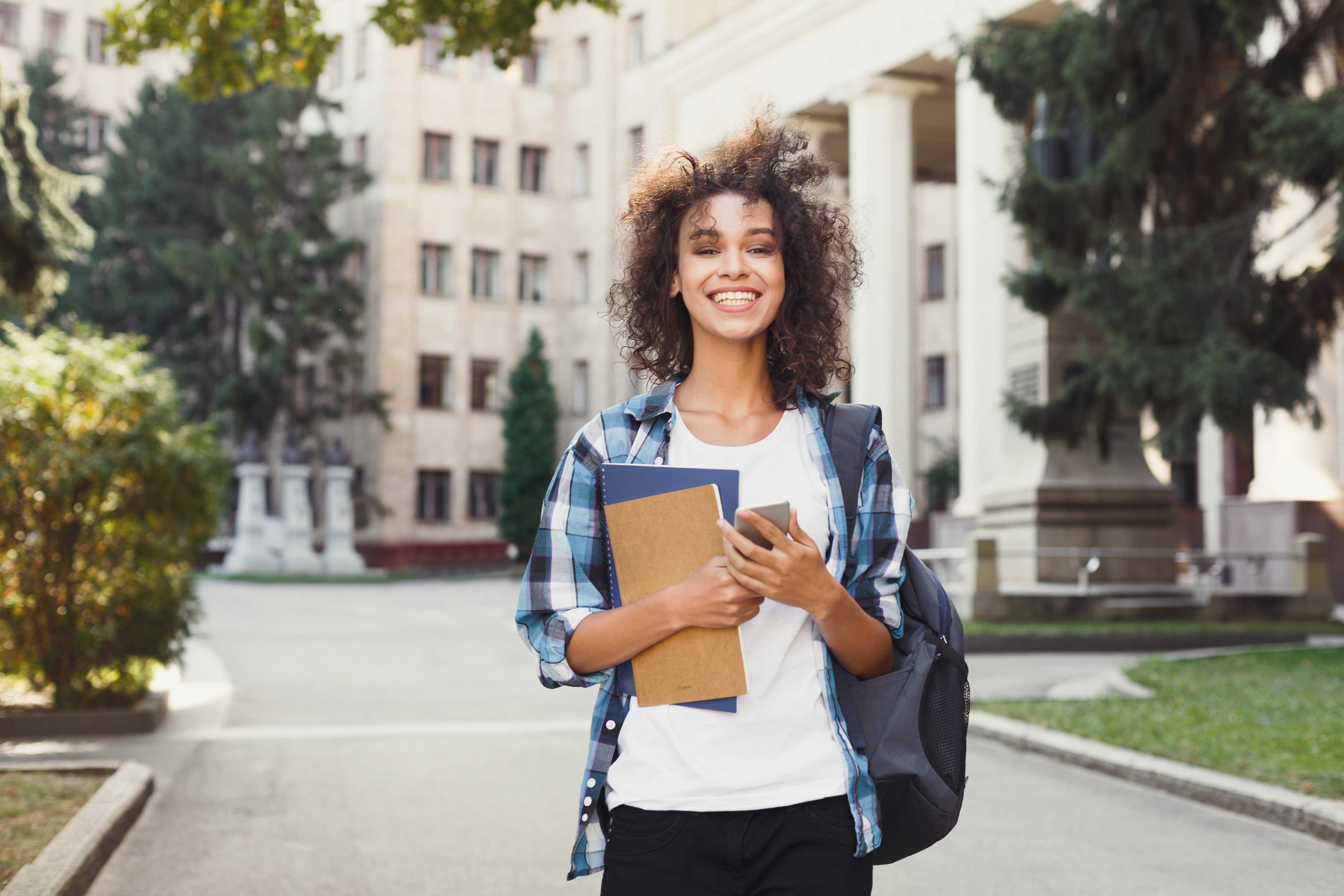 student-smiling-on-campus-holding-notebooks